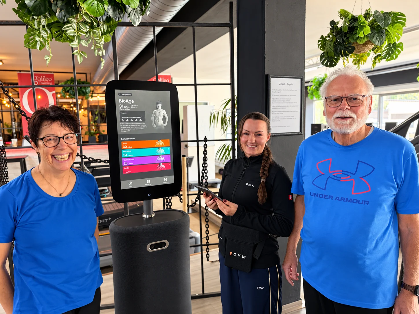 Ältere Trainierende mit ihrer Trainerin am EGYM-BioAge-Terminal im Gesundheitsstudio Wolff